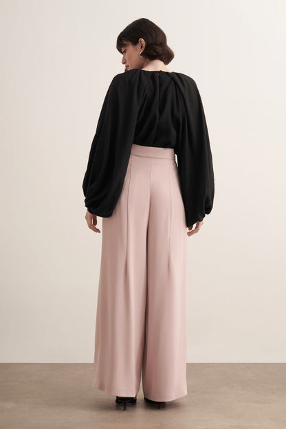 Cherianne.com high-waisted wide-leg trousers in beige with pleated detailing and side pockets worn by a model.