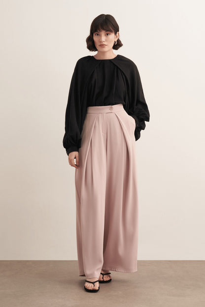 Cherianne.com high-waisted wide-leg trousers in beige with pleated detailing and side pockets worn by a model.