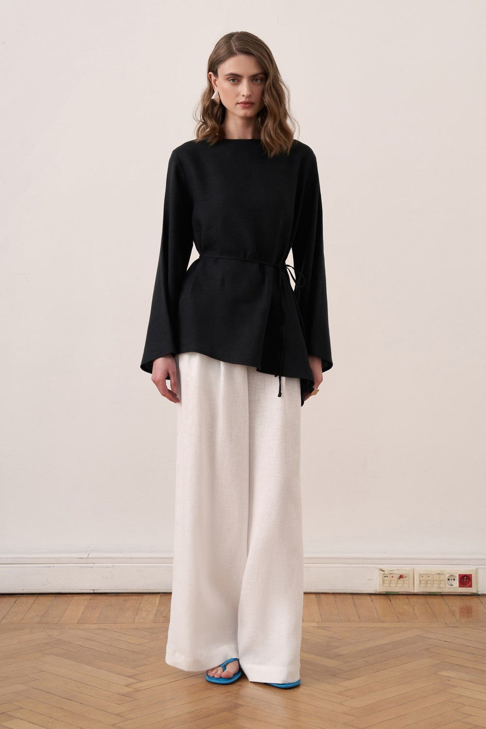Cherianne.com black linen blouse with wide sleeves and waist tie, paired with white wide-leg trousers on a model.