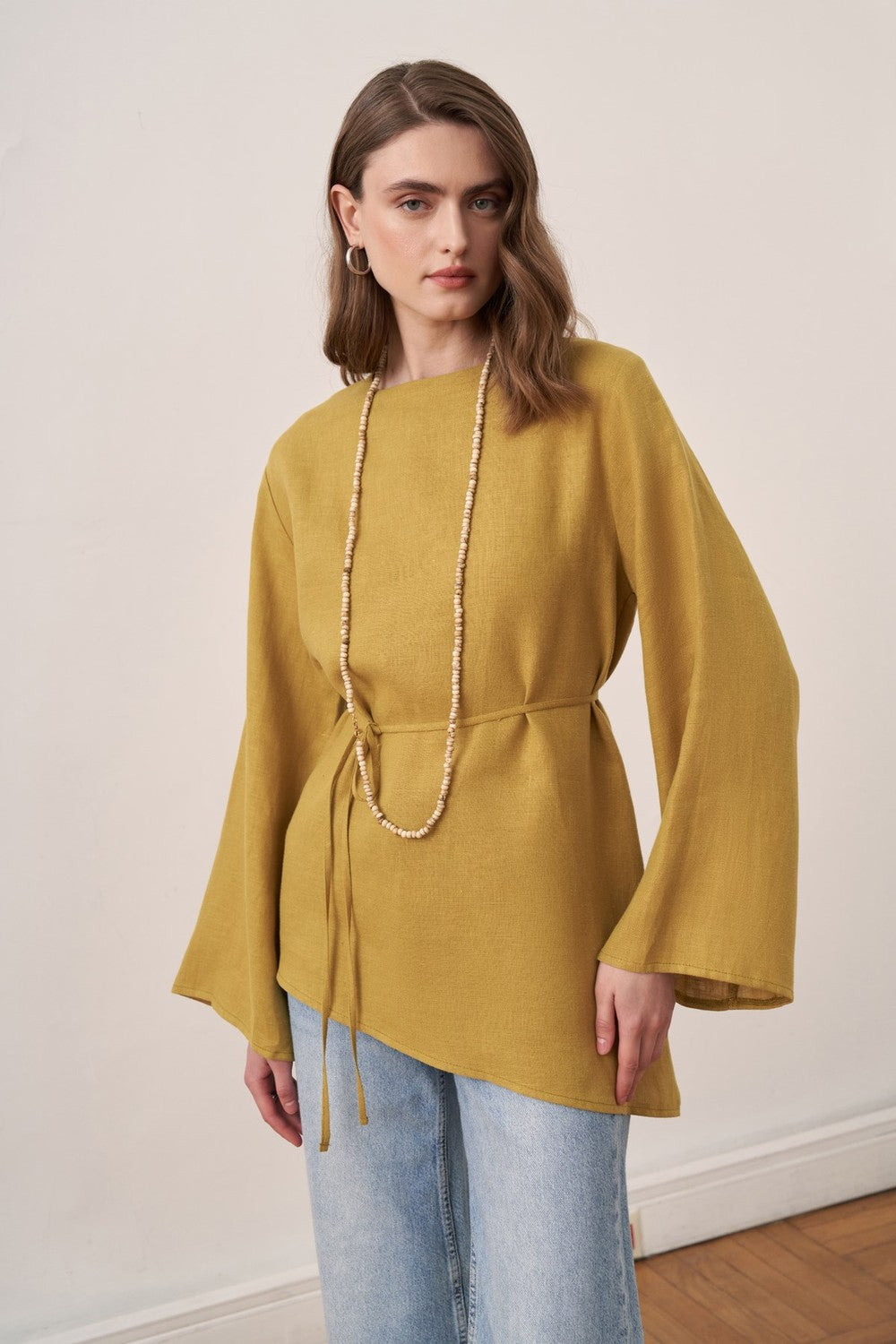 Cherianne.com wheat-colored linen blouse with wide bell sleeves and asymmetrical hem worn by a model with jeans.