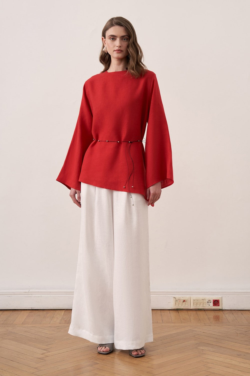 Cherianne.com red linen blouse with wide sleeves and waist tie paired with white wide-leg linen trousers on a model