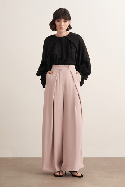 Cherianne.com high-waisted wide-leg trousers in beige with pleated detailing and side pockets worn by a model.