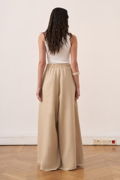Cherianne.com beige wide-leg linen trousers with an elasticated waistband worn by a model with a white tank top
