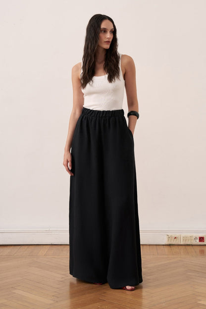 Cherianne.com black wide-leg linen trousers with an elasticated waist and side pockets worn by a model.