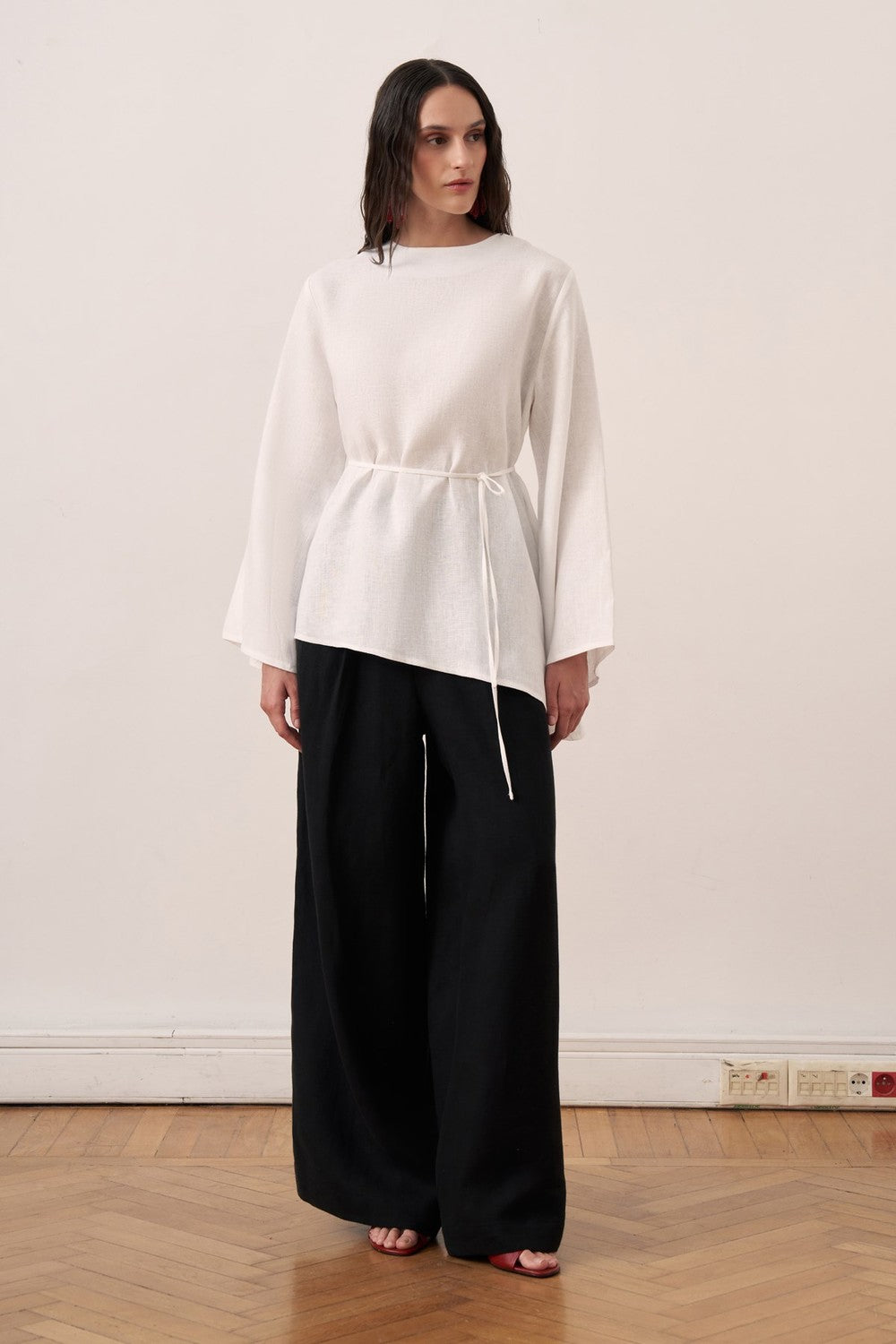 Cherianne.com wheat-colored linen blouse with wide bell sleeves, waist tie, and asymmetric hem worn with black pants.