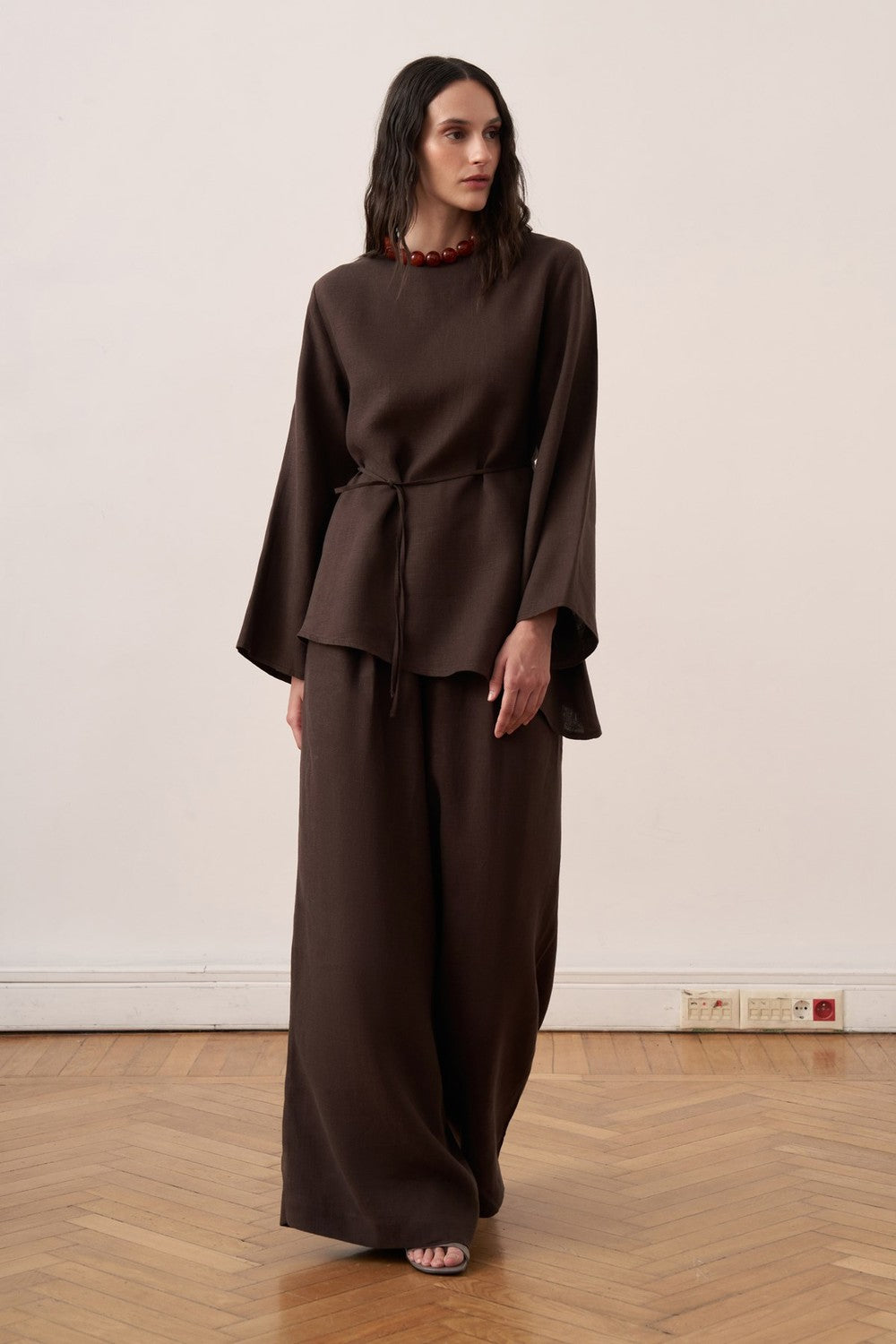 Cherianne.com dark brown linen blouse with wide sleeves, crew neck, and adjustable waist tie on a model.