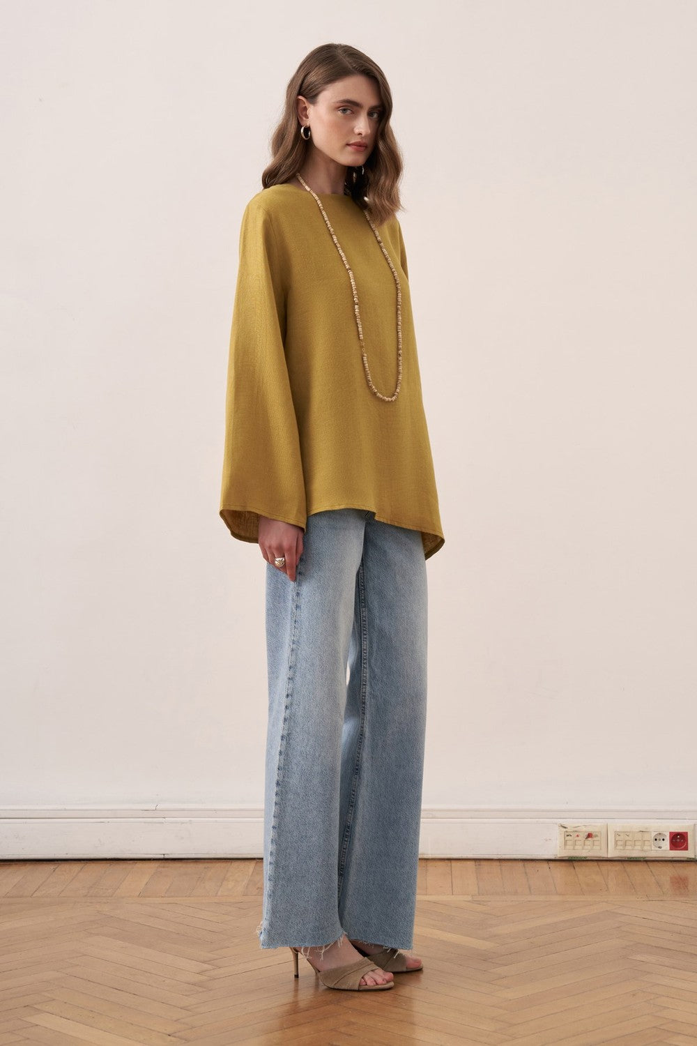 Cherianne.com wheat-colored linen blouse with wide bell sleeves and asymmetrical hem worn by a model with jeans.