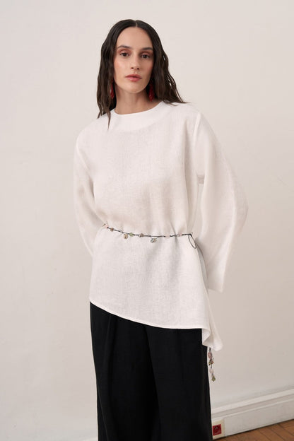 Cherianne.com wheat-colored linen blouse with wide bell sleeves, waist tie, and asymmetric hem worn with black pants.