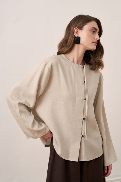 Cherianne.com beige linen shirt with mandarin collar, asymmetric button placket, and long sleeves on a model.
