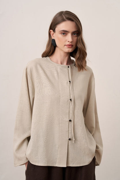 Cherianne.com beige linen shirt with mandarin collar, asymmetric button placket, and long sleeves on a model.