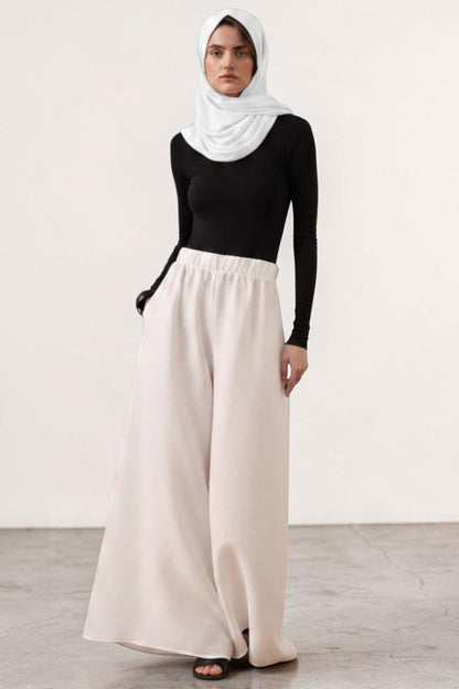 Cherianne.com wide-leg beige linen trousers with an elastic waistband, worn by a model in a black top and white hijab.
