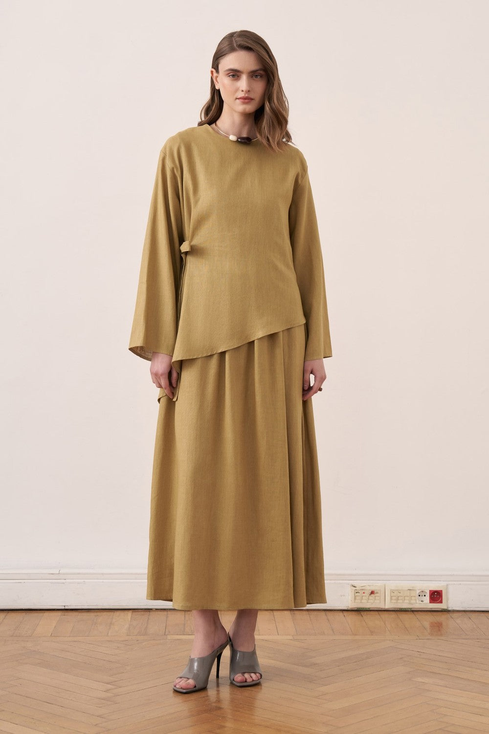 Model wearing a mustard yellow Cherianne.com two-piece linen blend dress set with an asymmetric tunic and maxi skirt.