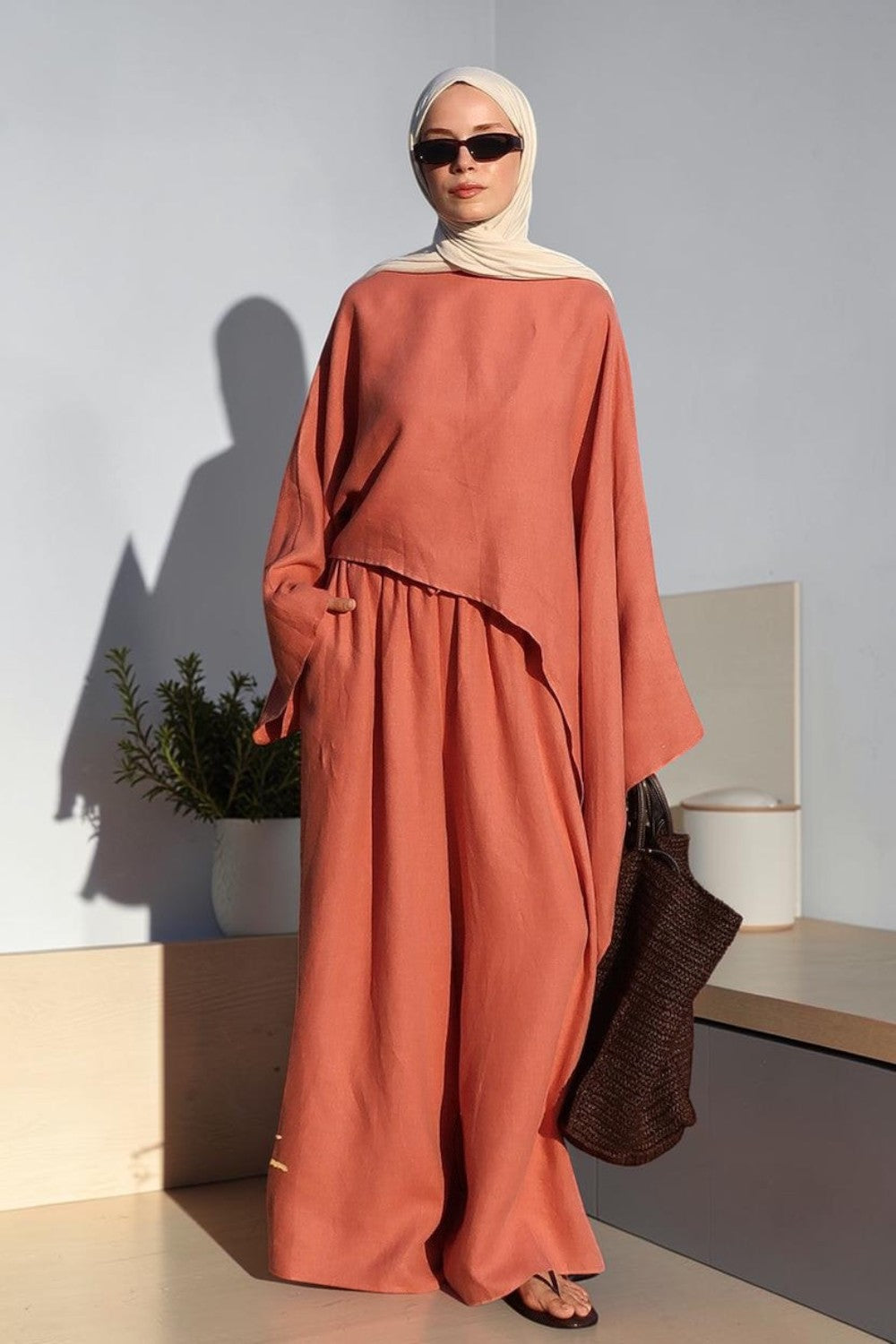 Cherianne.com terracotta oversize linen blouse with asymmetric cut worn by a woman with a beige hijab by the sea.