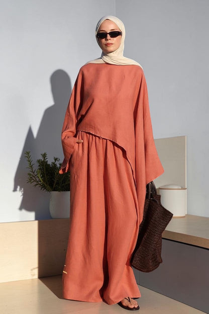 Cherianne.com terracotta oversize linen blouse with asymmetric cut worn by a woman with a beige hijab by the sea.