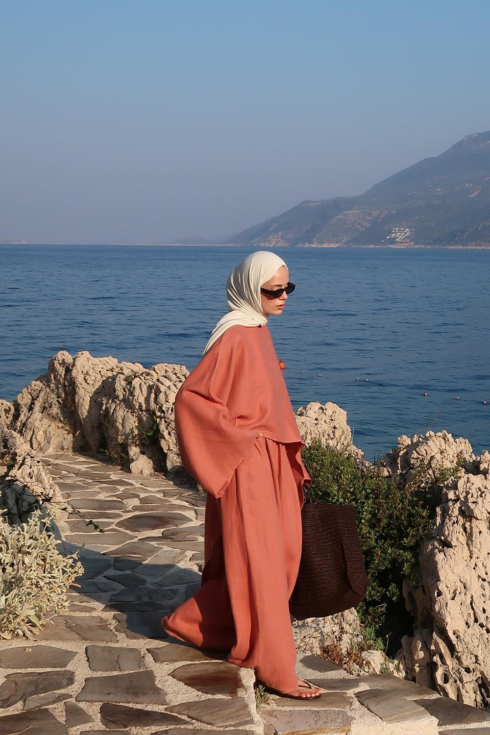 Cherianne.com terracotta oversized linen blouse with an asymmetric cut worn by a woman in a coastal setting