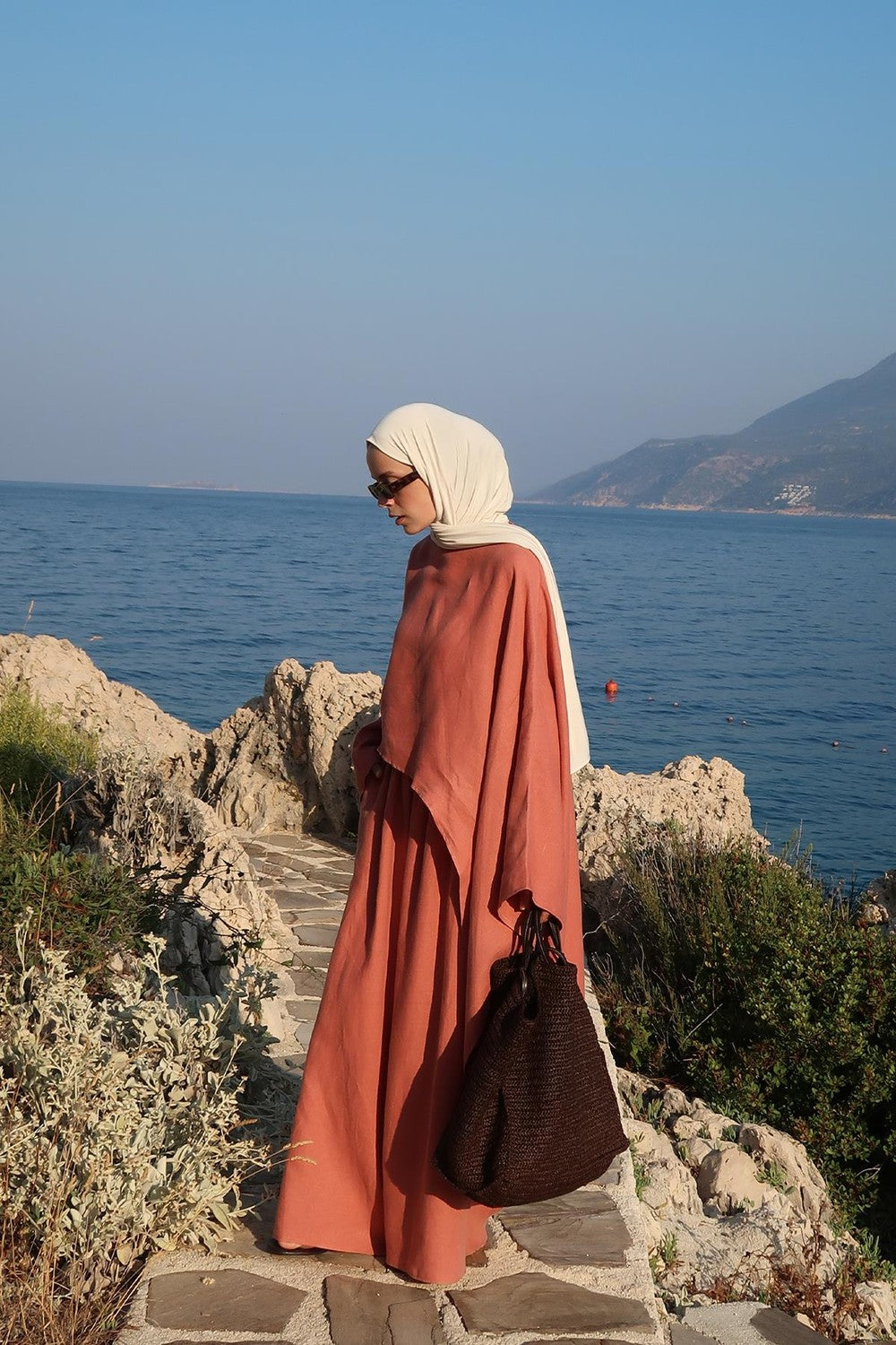 Cherianne.com terracotta linen blouse with an oversized, asymmetric cut worn by a model near the sea.