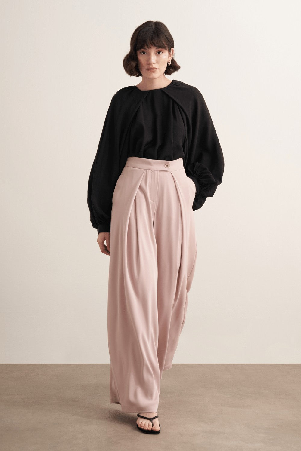 Cherianne.com high-waisted wide-leg trousers in beige with pleated detailing and side pockets worn by a model.