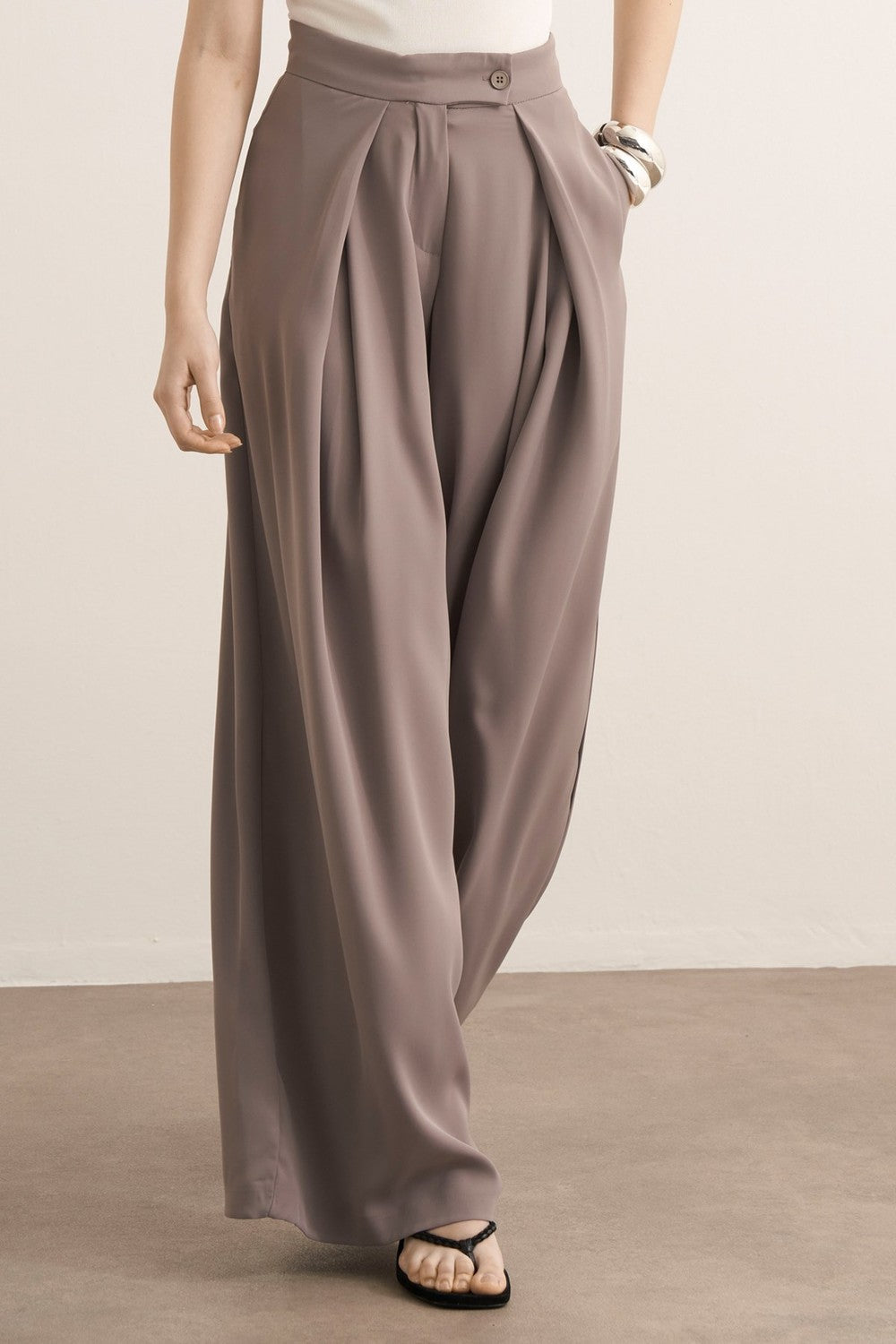 Cherianne.com Leona high-waisted wide-leg trousers in taupe with pleated details and side pockets on a model.