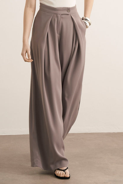 Cherianne.com Leona high-waisted wide-leg trousers in taupe with pleated details and side pockets on a model.